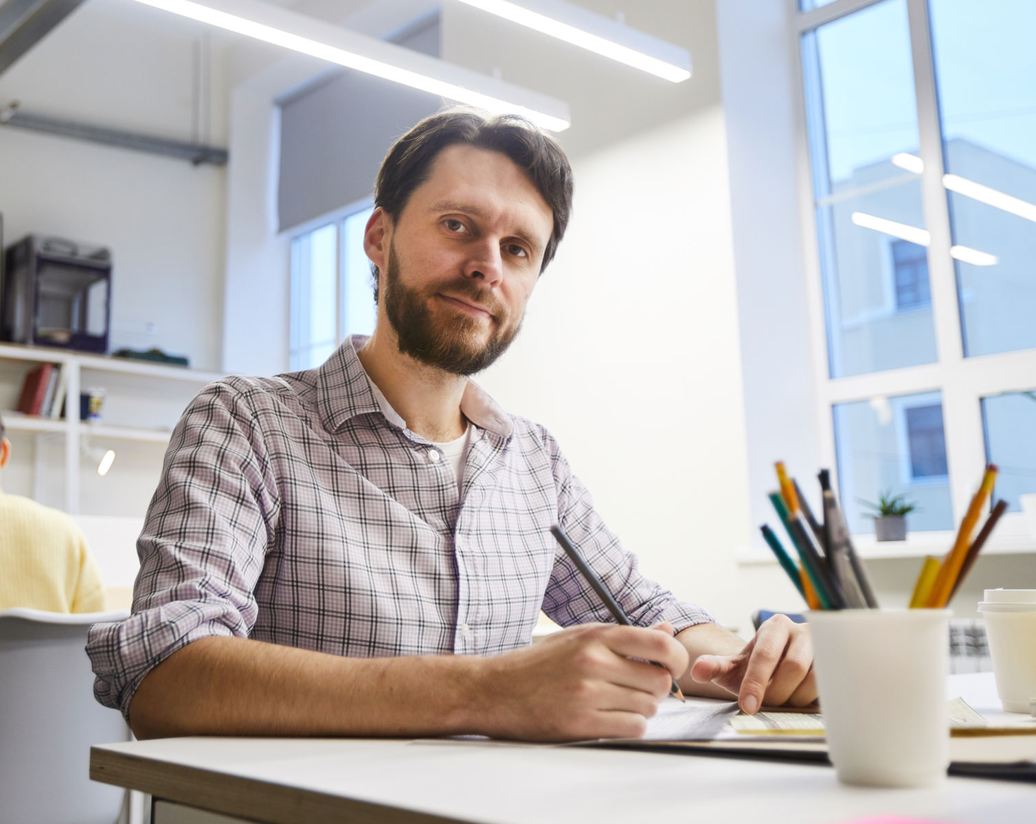 一位留着胡子的男子坐在办公室的办公桌前，为外贸建站制定数字营销和谷歌 SEO 策略。