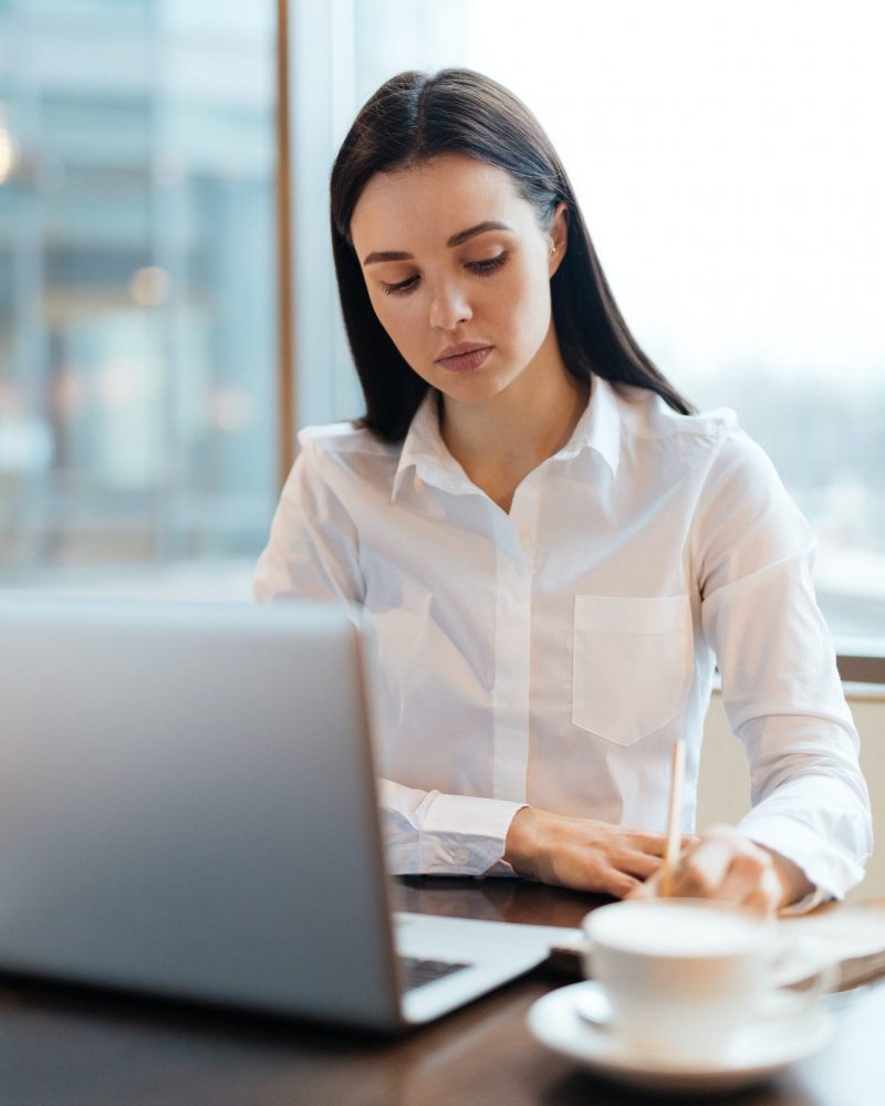 描述：一个女人坐在桌子前面，手里拿着一台笔记本电脑和一杯咖啡。